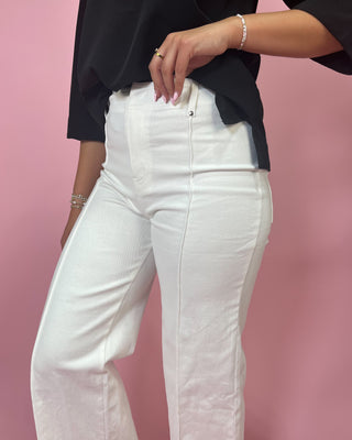 Person wearing white pants and a black top against a pink background