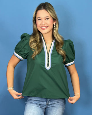 A woman modeling a dark green puff-sleeve top with a light blue and white V-neck trim, paired with blue jeans