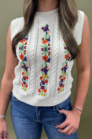 White sleeveless sweater with colorful floral embroidery worn by a person against a neutral background