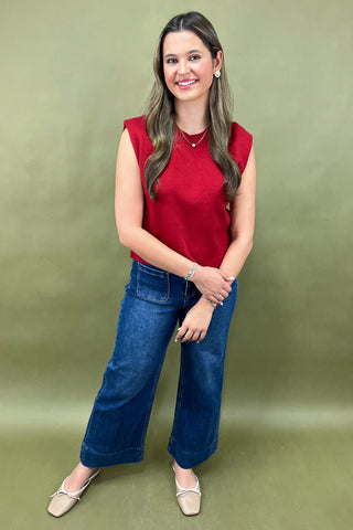 Woman wearing a red sleeveless top and blue jeans against a green background