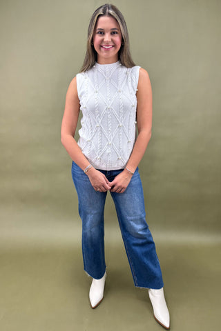 Woman wearing a white sleeveless top and blue jeans against a green background