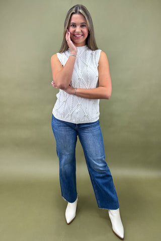 Woman wearing a white sleeveless top and blue jeans against a green background