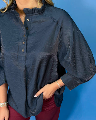 Navy satin blouse with a ruffled mock neckline, partial button front, and relaxed three-quarter sleeves.