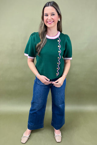 Woman wearing a green blouse with a decorative pattern and blue jeans on a green background