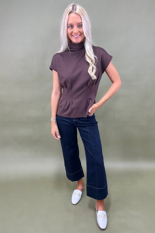 Woman wearing a brown top and blue jeans against a plain background