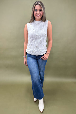 Woman wearing a white sleeveless top and blue jeans against a green background