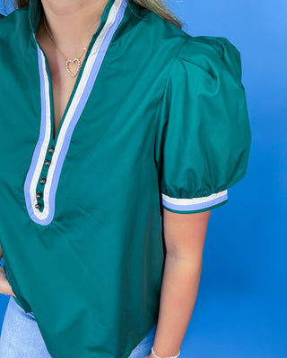 A close-up of a woman wearing a teal green short-sleeve blouse with a split V-neckline trimmed in white and light blue stripes