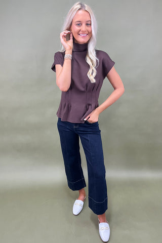Woman wearing a brown top and blue jeans against a plain background