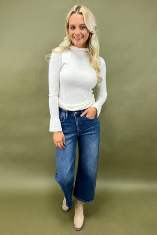 Woman wearing a white turtleneck sweater and blue jeans against a green background