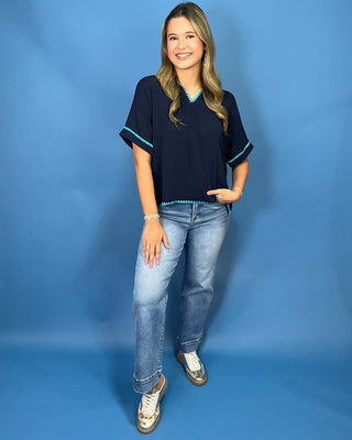 A woman modeling a navy blue short-sleeve top with turquoise trim, paired with light-wash jeans and white sneakers
