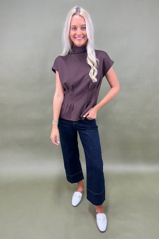 Woman wearing a brown top and dark blue jeans against a plain background