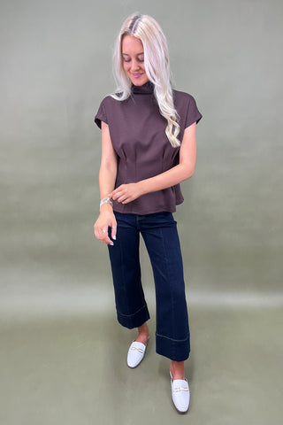 Woman wearing a brown top and dark blue jeans against a plain background