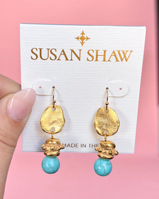 Gold and turquoise earrings on a Susan Shaw branded card against a pink background