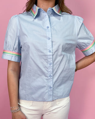 Light blue shirt with colorful trim worn by a person on a pink background