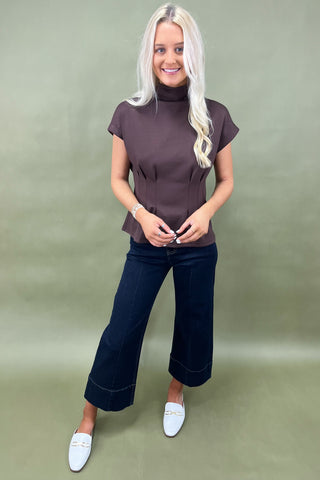 Woman wearing a brown top and dark blue jeans against a green background