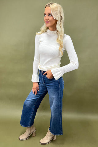 Woman wearing a white long-sleeve top and blue jeans against a green background