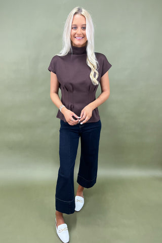 Woman wearing a brown top and dark blue jeans against a green background