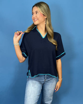 A woman modeling a navy blue short-sleeve top with turquoise trim, paired with light-wash jeans