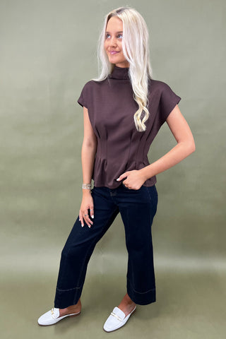 Woman wearing a brown top and dark jeans against a green background
