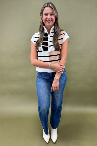Woman wearing a sleeveless striped top and blue jeans against a green background