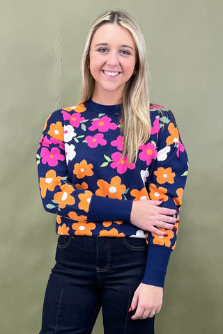 Woman wearing a navy sweater with colorful floral pattern against a green background