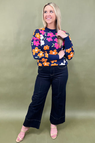 Woman wearing a colorful floral sweater and dark jeans against a green background