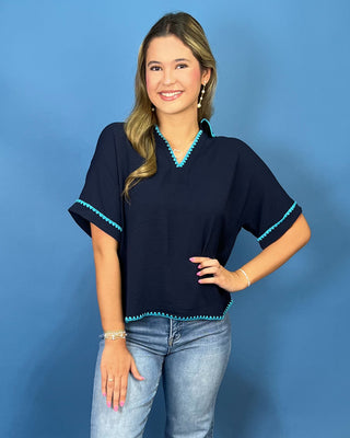 A woman modeling a navy blue short-sleeve top with turquoise trim, paired with light blue jean