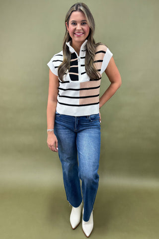 Woman wearing a black and white striped sleeveless top with blue jeans on a green background