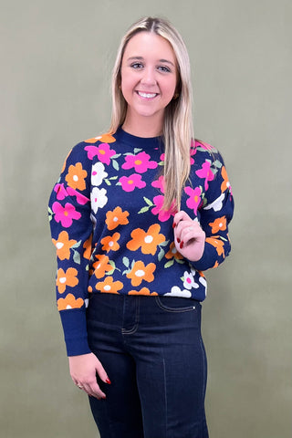 Woman wearing a navy sweater with colorful floral pattern against a plain background