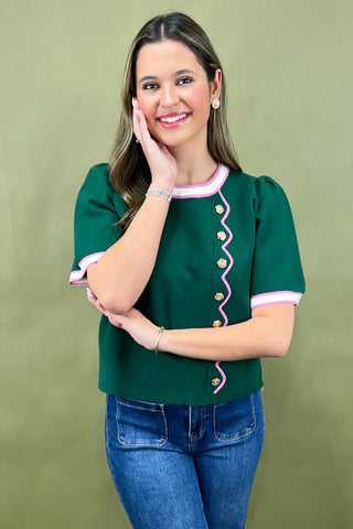 Woman wearing a green blouse with pink accents and blue jeans against a green background