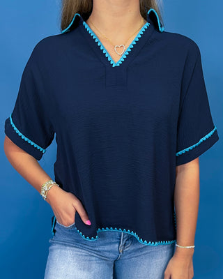A woman wearing a navy blue short-sleeve blouse with bright turquoise blue scalloped trim along the V-neck, sleeve cuffs, and hem