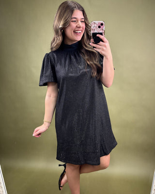 Woman taking a mirror selfie wearing a black dress against a green background
