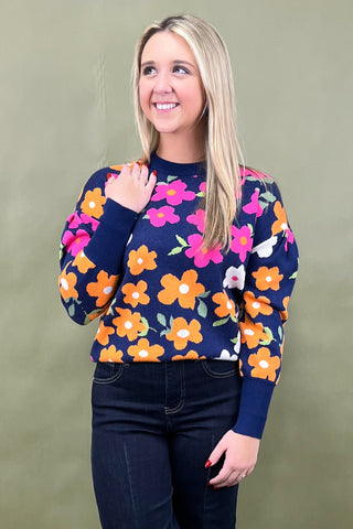 Woman wearing a navy sweater with colorful floral pattern against a green background