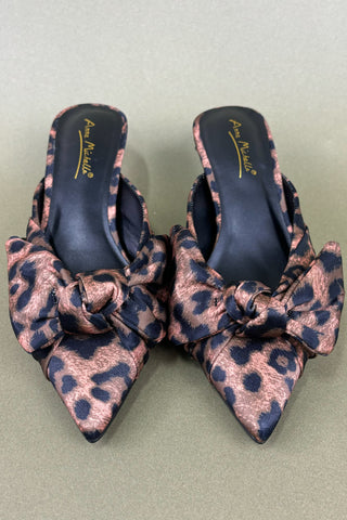 Pair of leopard print shoes with bow details on a light green background
