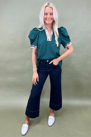 Woman wearing a green top with puff sleeves and dark blue jeans on a plain background