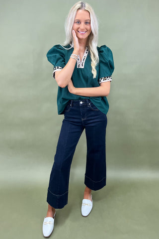 Woman wearing a green top and dark blue jeans on a green background