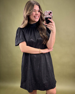 Woman taking a selfie wearing a black dress against a green background