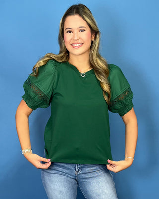 A woman modeling a dark green short-sleeve top with sheer puff sleeves and lace detailing on the cuffs