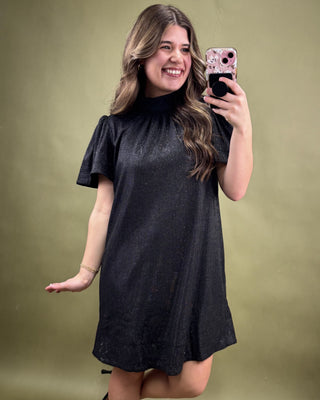 Woman wearing a black dress taking a selfie against a green background