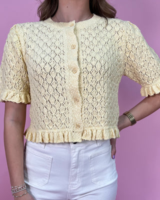 Person wearing a yellow lace cardigan against a purple background