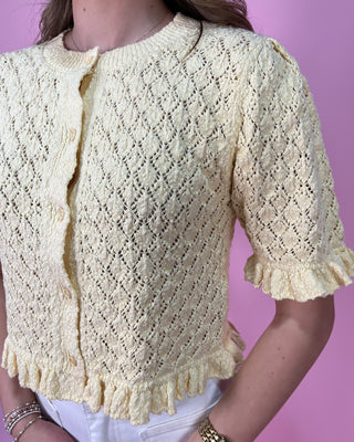 Light yellow knitted cardigan with a textured pattern on a pink background