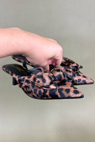 Leopard print shoes with bows held by a hand on a light gray background