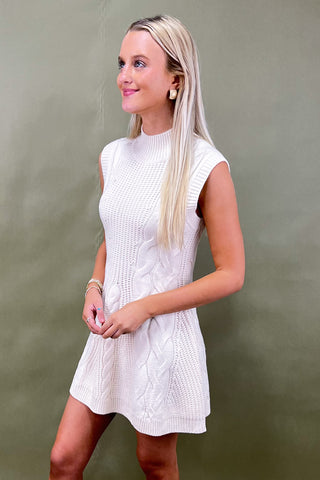 Woman wearing a white knitted dress against a plain background