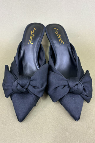 Pair of navy blue shoes with large bows on a beige background