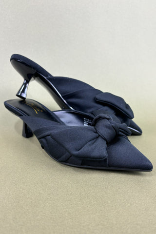 Black high-heeled shoes with bow detail on a beige background