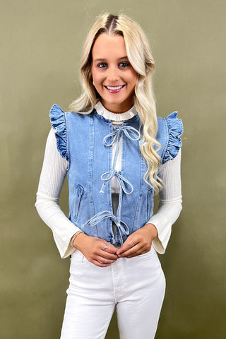 Woman wearing a denim vest with ruffled sleeves and a white top against a green background