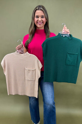 Woman holding two sweaters, one beige and one green, against a plain background