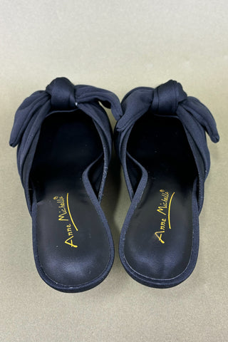 Pair of black sandals with bow details on a beige background