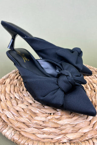 Black high-heeled shoes with bow details on a woven surface