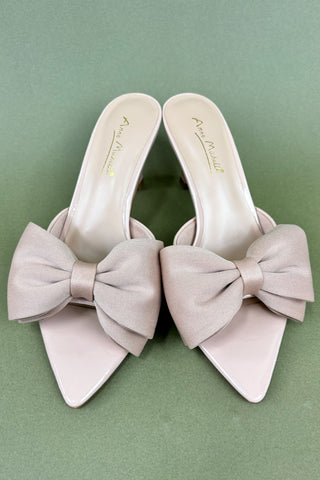 Pair of light pink high heels with large bows on a green background
